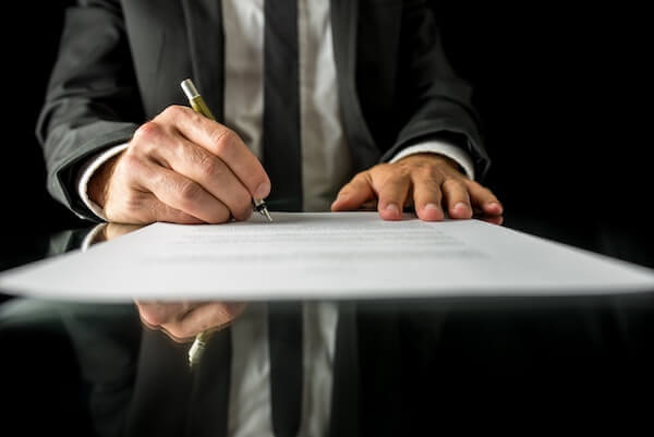 Front view of businessman signing important legal document for a bail bond on black desk with reflection. 